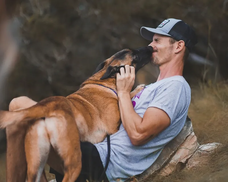 An Austin Dog Culture trainer sitting in the grass with a relaxed shepherd mix